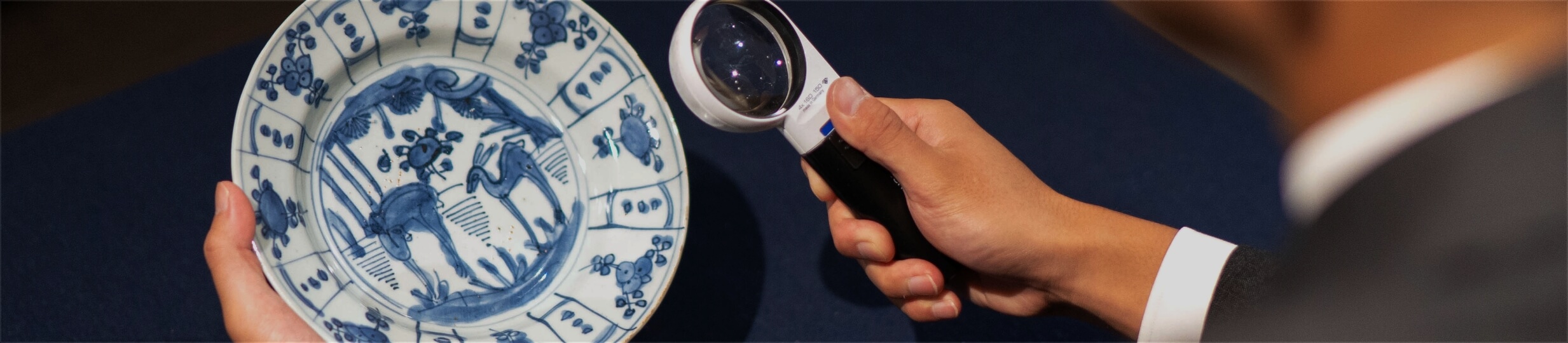 ルーペで青い絵付けの器を見る鑑定士