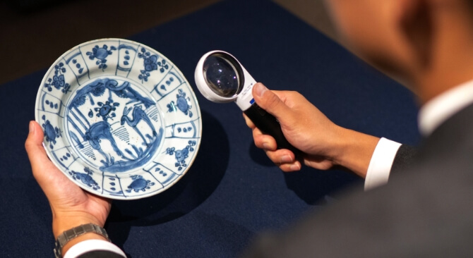 ルーペで青い絵付けの器を見る鑑定士