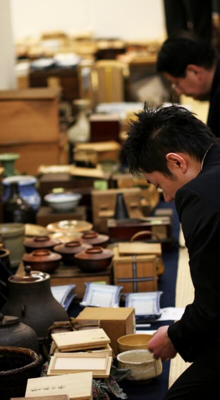 並んだ美術品・骨董品を見るスーツの男性