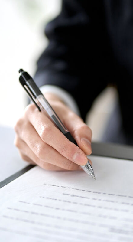 ボールペンで書類を書いているスーツの男性